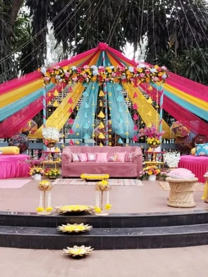 We love bringing vibrant traditions to life. This colorful Mehendi ceremony setup features a canopy of multi-hued drapes, bright floral arrangements, and comfortable, festive seating, creating the perfect backdrop for a joyous celebration.