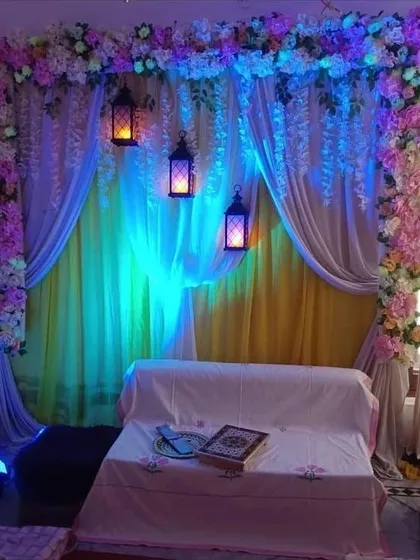 An intimate indoor ceremony backdrop created with layers of drapes and floral borders. Hanging lanterns and colored uplighting are used to create a warm and magical ambiance, perfect for an evening sangeet or nikah ceremony.