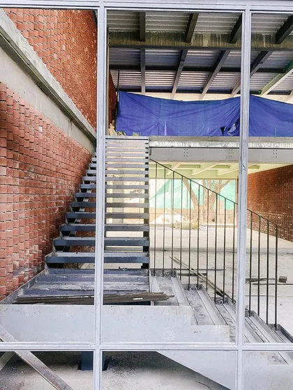 A view through a window frame during construction, showing the relationship between the brick wall and the steel staircase.