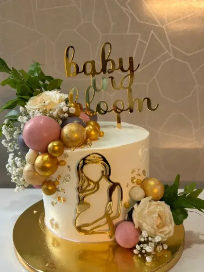 A "Baby in Bloom" themed cake for a modern baby shower. The design features an elegant silhouette, fresh-looking flowers, and a cascade of pink and gold spheres.