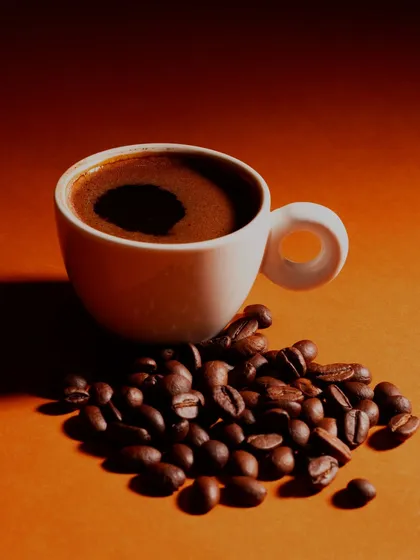 A minimalist shot of a cup of black coffee and scattered beans. The warm, gradient lighting creates a rich and inviting mood.