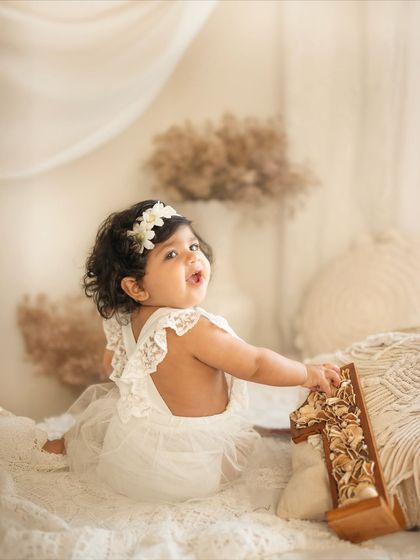 A beautiful back view of this little girl in her lace romper, looking over her shoulder with a sweet smile during her boho-themed first birthday shoot.