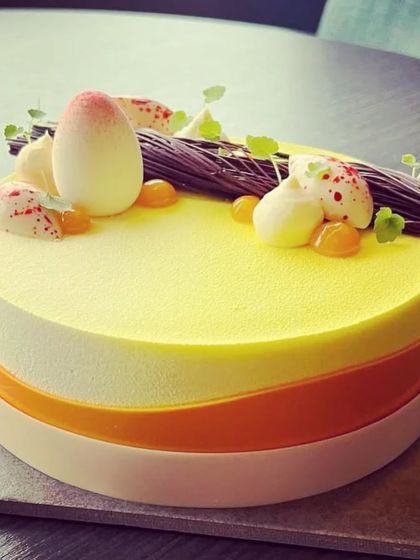 A modern entremet cake with a yellow velvet finish. The cake is decorated with white chocolate eggs and a chocolate branch, showcasing our pastry team's skill.