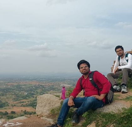 Two trekkers taking a break on the trail during the Adiyogi trip, with a vast landscape stretching out before them.