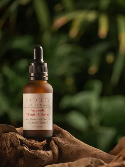 An ayurvedic vitamin C serum resting on a piece of driftwood against a lush, green background. This composition emphasizes the product's natural, plant-based origins.