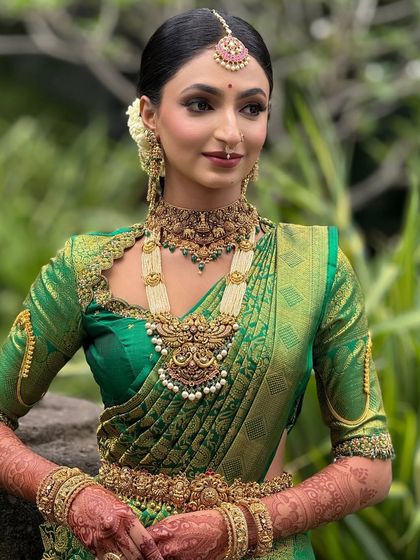 A detailed shot of the bride's makeup and jewelry. The focus is on creating a radiant complexion and defining the eyes to complement the heavy temple jewelry.