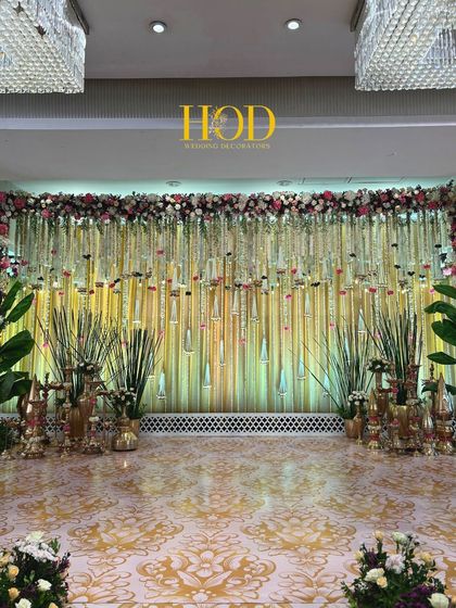 A classic and elegant wedding stage with a backdrop of shimmering gold drapes and a ceiling of hanging floral strings and glass droplets, flanked by traditional brass decor.