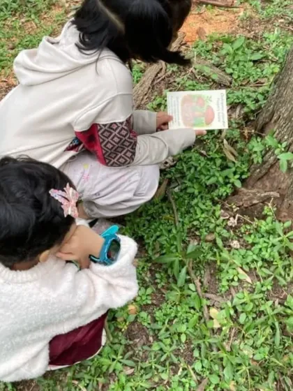 Two young girls crouch down to get a better look at a mushroom, using a book for reference. Our walks encourage teamwork and shared learning among friends.