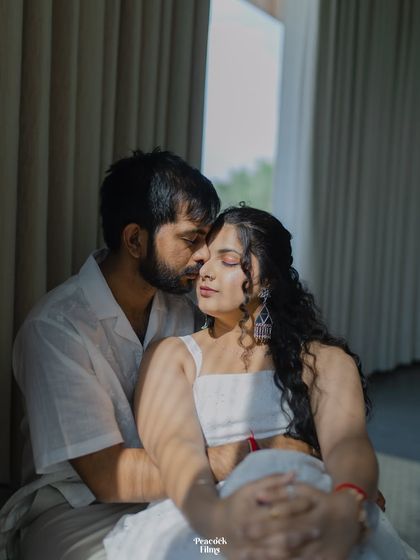 An intimate pre-wedding portrait, with soft light filtering through the curtains. This frame captures a tender kiss on the forehead, a silent promise of care and affection.