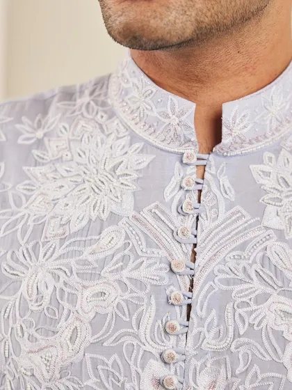 A close-up of the neckline of the lavender kurta, showing the detailed floral embroidery and fabric-covered buttons.