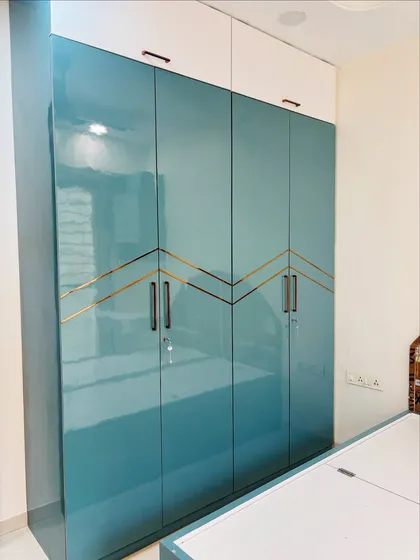 This glossy teal wardrobe with gold inlay detailing adds a pop of color and luxury to the bedroom. The two-tone design with white overhead cabinets makes the ceiling appear higher.