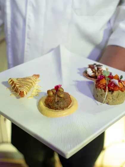 A chef holds up a square plate showcasing a sampler of four different appetizers, each a miniature work of art.
