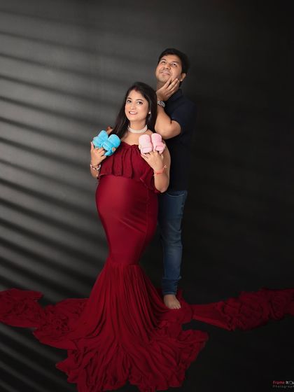 A playful and creative maternity photo. The mom-to-be holds up one pink and one blue bootie, adding a fun "guess what it will be" element to her shoot.