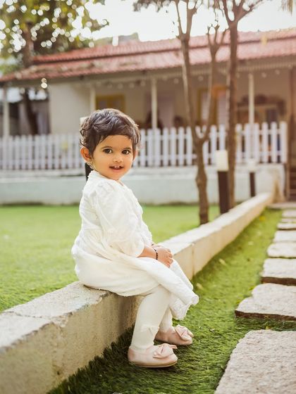 A sweet little girl sitting on a wall in a beautiful garden setting. Outdoor sessions are perfect for capturing kids in their element.