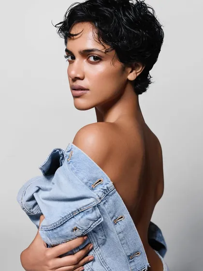 A minimalist and confident shot. The styling is simple, with the denim jacket worn off the shoulder to create a strong line and highlight the model's bare back and sharp haircut.