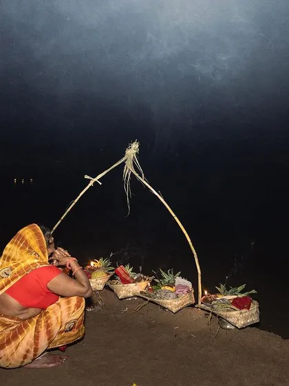 A woman arranges her offerings on the riverbank at night. This image focuses on the intricate details and preparations that are part of the Chhath festival.