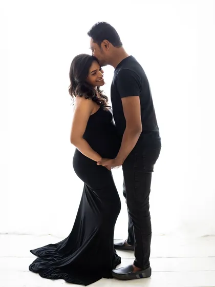 A tender moment between the couple, both dressed in black. His gentle kiss on her forehead speaks volumes in this simple yet powerful maternity portrait.