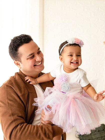 A father and daughter share a laugh during a studio session. The bright, high-key lighting creates a joyful and energetic feel.