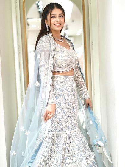 A full, smiling shot of the white and silver fish-cut lehenga. The attached jacket-style dupatta adds a layer of elegance to this modern silhouette.