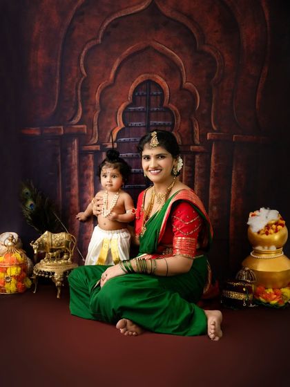 A full-length portrait of Yashoda and Krishna against a temple backdrop, surrounded by props like peacock feathers and a pot of butter.