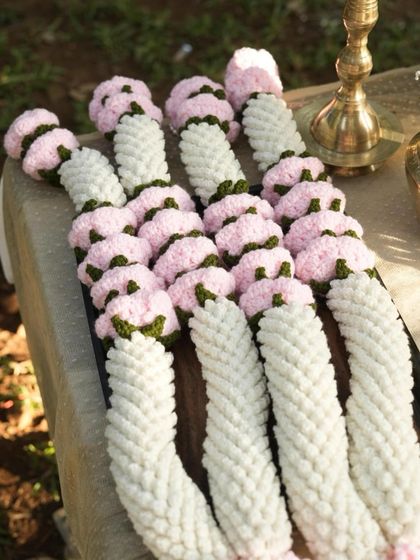A close up look at the detail and texture of a finished crochet varmala before it gets shipped out. You can see the tightly woven white yarn that forms the base and the individually crafted pink flowers with green leafy accents.