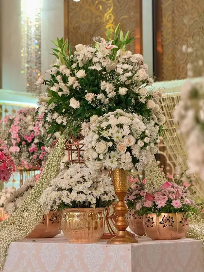 Regal details and florals that bloom with charm. This towering arrangement of white flowers in a golden urn is a timeless ode to elegance. ✨