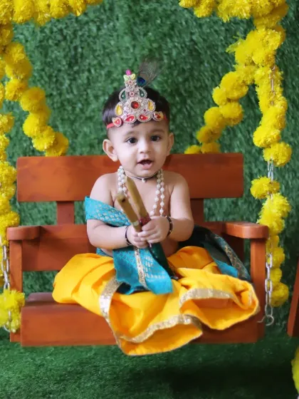A regal pose from a baby Krishna, holding his flute on a decorated swing. The rich colors and textures in this setup create a stunning final portrait.