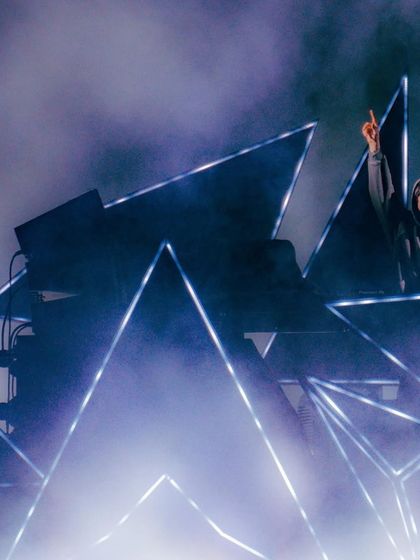 Alan Walker stands atop his custom geometric stage, pointing to the sky amidst a haze of atmospheric smoke.