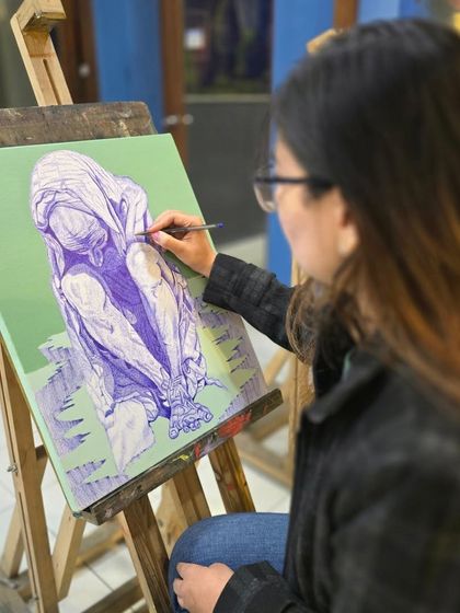 A student works on a figurative drawing using a ballpoint pen, capturing the form and shadows of a huddled figure in this powerful piece.