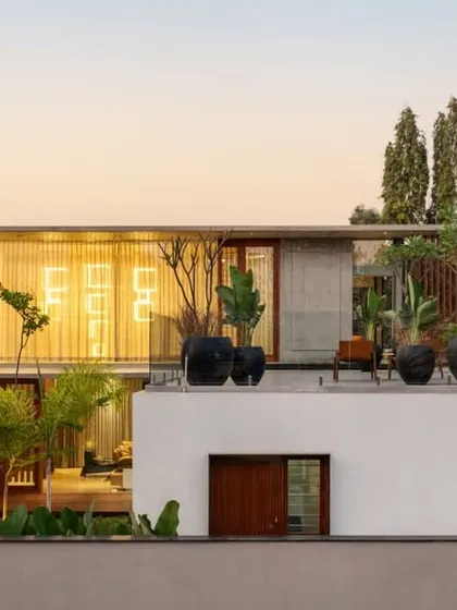 The rear elevation of the Long House at sunset, showing the relationship between the different volumes. The upper terrace, adorned with potted plants, becomes an elevated garden with views of the surroundings.