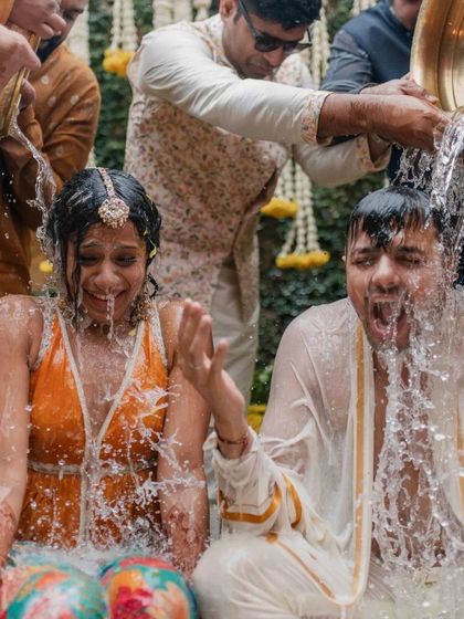 Even a downpour couldn't stop this Haldi. This shot captures the exact moment the couple gets drenched with water, their expressions of shock and laughter showing their amazing spirit.