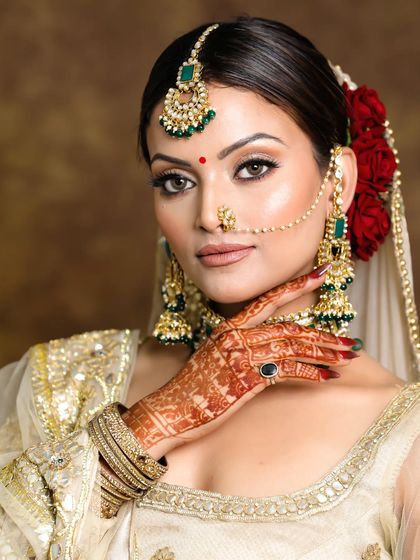 A beautiful portrait of my bride, showcasing her intricate henna and the glowing makeup look we designed. The emerald jewelry adds a perfect pop of color against the golden outfit.