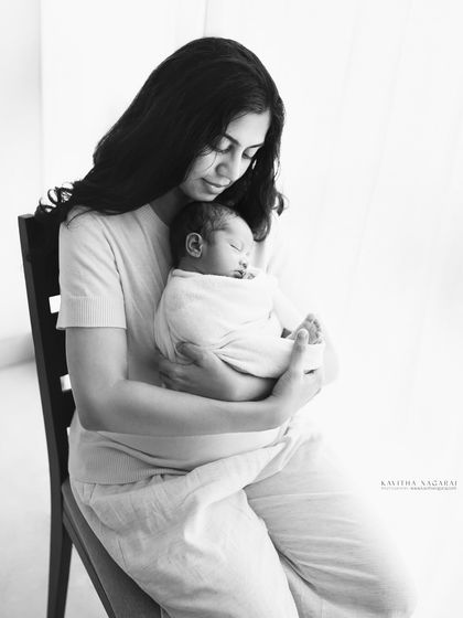 A mother holds her sleeping newborn, both bathed in soft, natural light. A serene and emotional portrait that speaks to the quiet moments of motherhood.