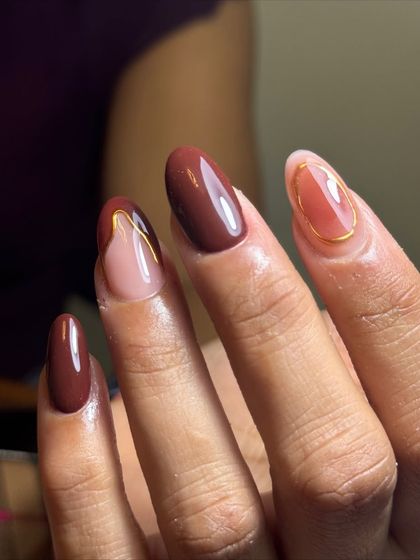 An elegant and moody design with a mix of solid brown nails and a negative space design with gold wire accents.