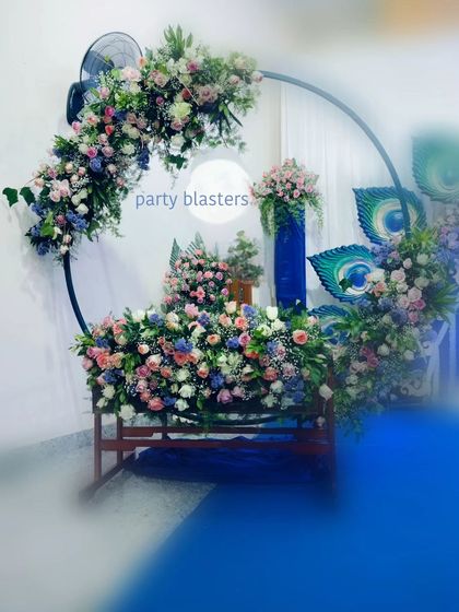 A closer look at the cradle area for a Krishna-themed naming ceremony. The circular arch is heavily decorated with a mix of pink, blue, and white flowers, creating a lush and beautiful frame for the baby's cradle.