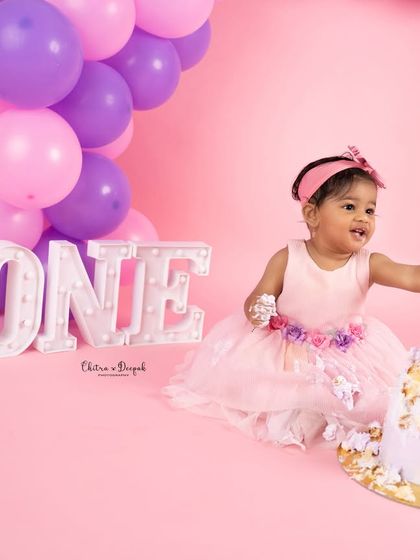 A playful moment captured during a pink-themed cakesmash session, as the birthday girl reaches for her cake with frosting-covered hands.