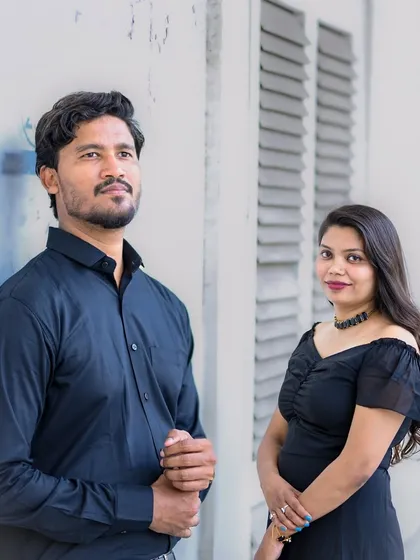 A stylish portrait of the couple posing individually but together in the frame, set against a white textured wall with vintage shutters.