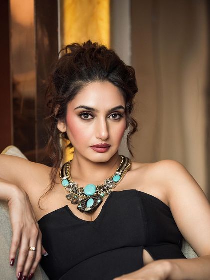 A classic, elegant portrait focusing on the subject's expression and a bold statement necklace. The soft lighting and relaxed pose create a look of authentic, effortless glamour.