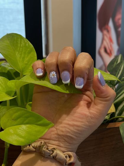 A single hand holding a leaf, giving you a detailed look at the delicate, hand-painted daisy on the accent nail.