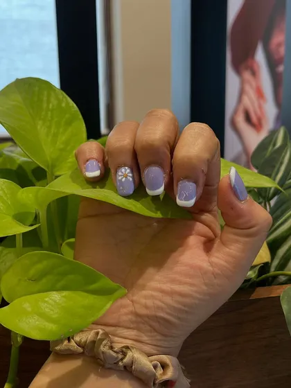 A single hand holding a leaf, giving you a detailed look at the delicate, hand-painted daisy on the accent nail.