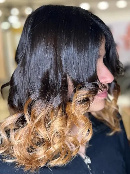 A classic ombre look with a dark base transitioning to blonde ends. The hair is styled in defined curls to showcase the color contrast.