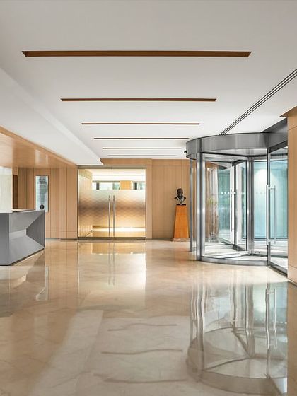 The main lobby of 'The Layered Office', showing the flow from the revolving door entrance past the reception desk. The use of polished marble and warm wood paneling creates a sophisticated and welcoming atmosphere.