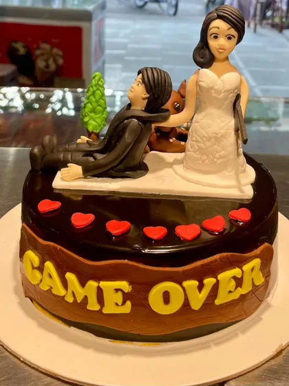 A humorous and expertly crafted "Game Over" bachelor party cake. This design features detailed fondant figures of the bride and groom, a rich chocolate glaze, and a playful theme that's perfect for celebrating the groom-to-be's next chapter.