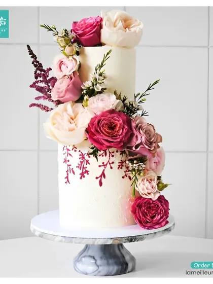 This elegant two-tiered cake showcases a beautiful cascade of fresh pink and cream roses. A touch of hand-painted floral detail on the bottom tier adds a unique, artistic element perfect for a sophisticated wedding or anniversary celebration.