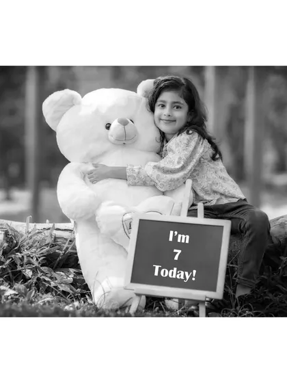 A quiet moment captured in monochrome. Brishka smiles as she hugs her large teddy bear, with the "I'm 7 Today!" sign adding context to this sweet seventh birthday photo.
