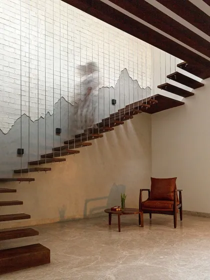 A floating staircase with wooden treads suspended by thin cables. The design is minimalist yet dramatic, with the wall behind featuring a textured, mountain-like contour, blending architectural precision with organic form.