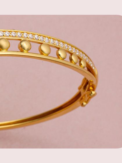 This gold kada features a unique design with a row of gold beads set alongside a channel of diamonds. The combination of textures creates a sophisticated and eye-catching look.