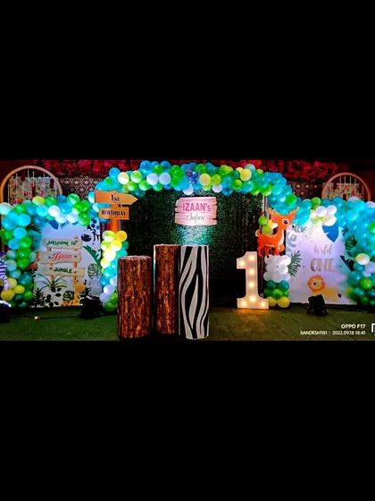 A "Wild One" jungle themed first birthday party. The outdoor setup on artificial grass includes a balloon arch, animal print pedestals, and a light-up number '1'.