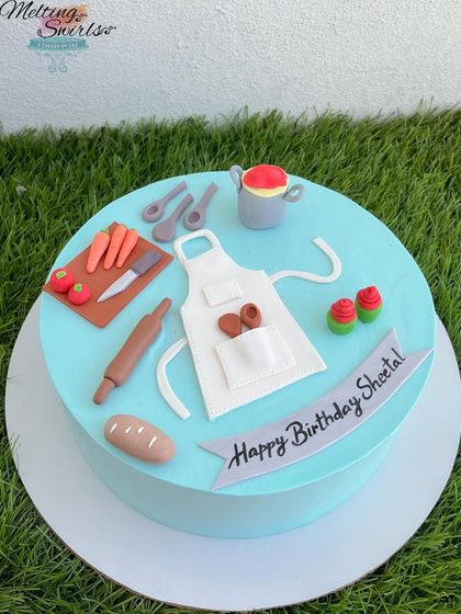 A cake for a chef's birthday, decorated with miniature, handmade fondant kitchen tools, an apron, and vegetables. It's a perfect tribute to someone passionate about cooking.