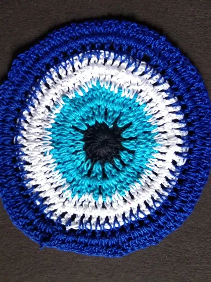 An evil eye doily that can also be used as a coaster or a wall hanging. It's a unique piece of home decor that's both stylish and protective.